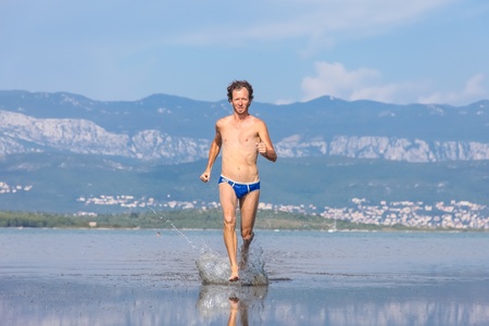 Man run across the beach in blue bathing suitの写真素材