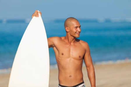 young man holding surfboard on beach in Baliの写真素材