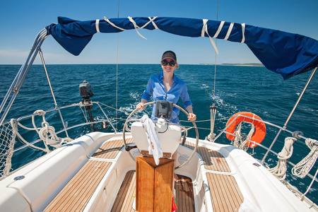 Young woman standing at the helm of a boat against a blue sky