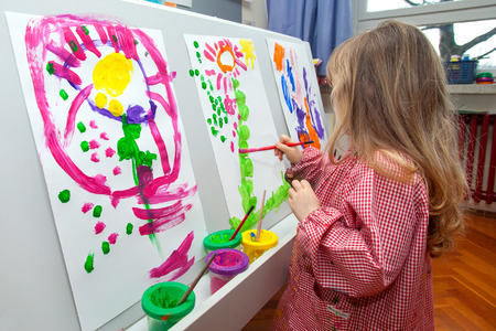 Cute little blond girl holding the brush and painting on the paperの写真素材