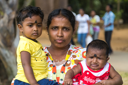 KANDY, SRI LANKA - FEBRUARY 26, 2014: Portrait of local woman holding two kids. Kandy is home of The Temple of the Tooth Relic, one of the most sacred Buddhist places of worship.のeditorial素材