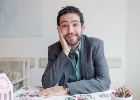 Happy young man wearing jacket sitting in restaurant and smiling.の写真素材