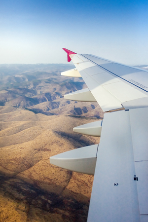 Airplane wing during flight above desert mountains.の写真素材