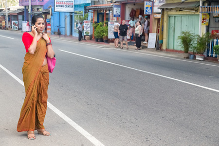 HIKKADUWA, SRI LANKA - FEBRUARY 24, 2014: Beautiful woman dressed in sari on phone on street. Around 45-50% of people in Sri Lanka own a mobile phone now.のeditorial素材