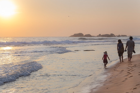 HIKKADUWA, SRI LANKA - FEBRUARY 24, 2014: Family walking on sandy beach at sunset. Hikkaduwa is very popular place for family vacationers.のeditorial素材