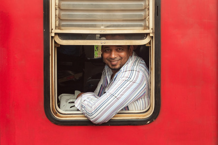HIKKADUWA, SRI LANKA - FEBRUARY 22, 2014: Smiling passenger framed in train window. No trains are air-conditioned so passengers just open the windows.のeditorial素材
