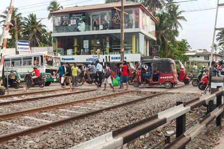 HIKKADUWA, SRI LANKA - FEBRUARY 22, 2014: Pedestrians and vehicles on rail crossing. All towns along the coast have a close relationship with the railway system.のeditorial素材