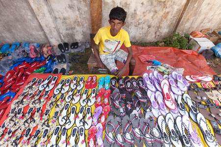 HIKKADUWA, SRI LANKA - FEBRUARY 23, 2014: Young local market vendor selling sandals. The Sunday market is great way to see local life come alive along with fresh produce and local delicacyのeditorial素材