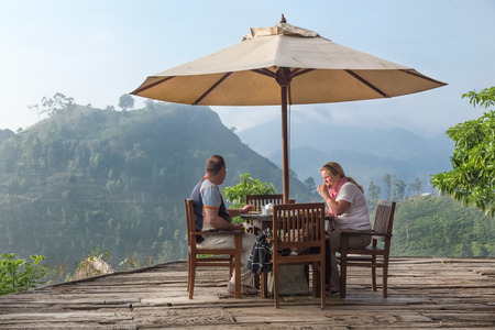 ELLA, SRI LANKA - MARCH 3, 2014: Tourist couple having breakfast at bungalow terrace with amazing view on tea plantations in background. Tea plantations are vital part of Sri Lankan economy since 1850のeditorial素材