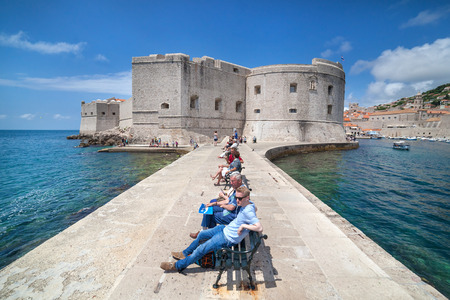 DUBROVNIK, CROATIA - MAY 27, 2014: Tourists sitting on bench on dock in front of the St. John fortress near the old port. Fortress houses the Maritime Museum and the aquarium.のeditorial素材