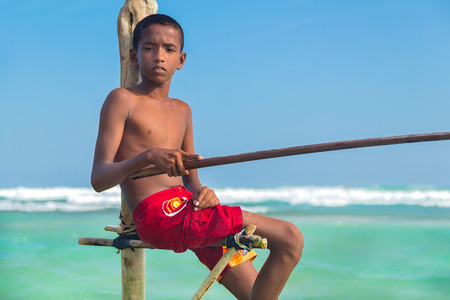 UNAWATUNA, SRI LANKA - MARCH 9, 2014: Young stilt fisherman at Hikkaduwa Beach. Most real stilt fishermen have been long gone. Today it's mainly young boys posing as stilt fishermen for tourists.のeditorial素材