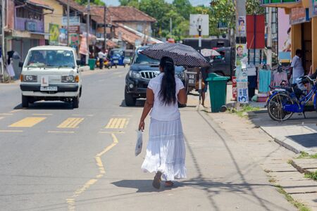 HIKKADUWA, SRI LANKA - MARCH 4, 2014: Local woman walking on the streets of  Hikkaduwa with opened umbrella. The sun is very strong and people prefer having lighter skin.のeditorial素材