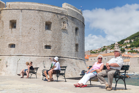 DUBROVNIK, CROATIA - MAY 27, 2014: Elderly couple  sitting on bench on dock in front of the St. John fortress near the old port. Fortress houses the Maritime Museum and the aquarium.のeditorial素材
