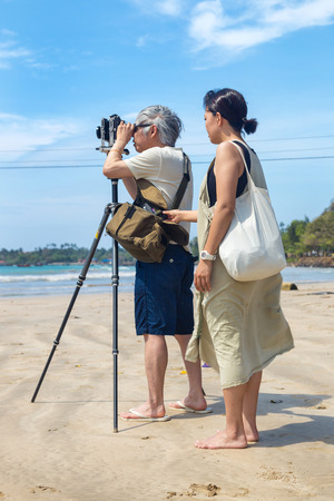 WELIGAMA, SRI LANKA - MARCH 7, 2014: Japanese tourists stand on sandy beach and take photos with old film camera. Tourism and fishing are two main business in this town.のeditorial素材