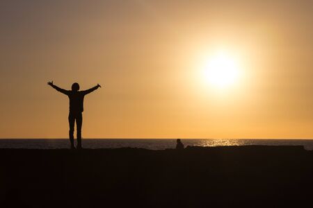 Silhouette of woman raising hands to sun at sunset.