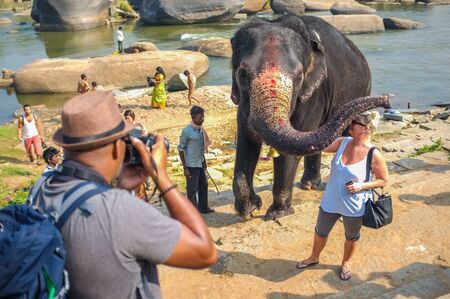 HAMPI, INDIA - 28 JANUARY 2015: Morning ritual of bathing Lakshmi. The temple elephant of Virupaksha Temple being photographed with tourists.のeditorial素材