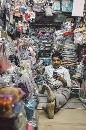 JODHPUR, INDIA - 07 FEBRUARY 2015: Store owner sits on floor of little textile shop overflown with different merchandise and waits for customers. Post-processed with added grain and texture.のeditorial素材