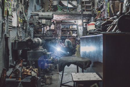 JODHPUR, INDIA - 17 FEBRUARY 2015: Mechanic welds metal part producing glare in background of...