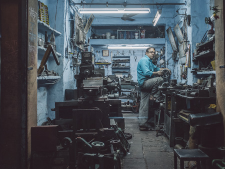 JODHPUR, INDIA - 17 FEBRUARY 2015: Mechanic working late in workshop with scattered equipment and...