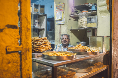JODHPUR, INDIA - 16 FEBRUARY 2015: Vendor sits in store with food on metal plates. Post-processed with grain and texture.のeditorial素材