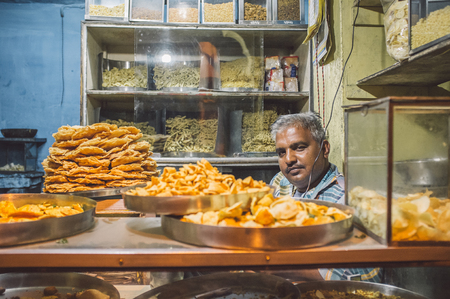 JODHPUR, INDIA - 16 FEBRUARY 2015: Vendor sits in store with various food on metal plates and noodles on shelves. Post-processed with grain and texture.のeditorial素材