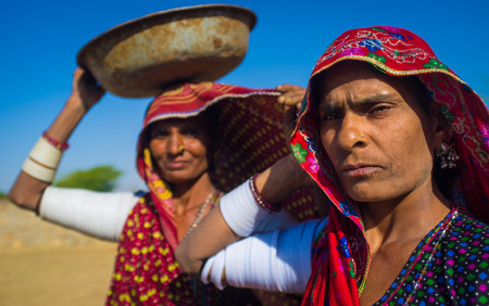 GODWAR REGION, INDIA - 14 FEBRUARY 2015: Rabari tribeswomen stand in field wearing sarees and upper-arm bracelets. One balances bucket on head. Rabari are an Indian community in the state of Gujarat.のeditorial素材