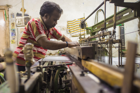 VARANASI, INDIA - 21 FEBRUARY 2015: Worker repairs textile machine in small factory.のeditorial素材