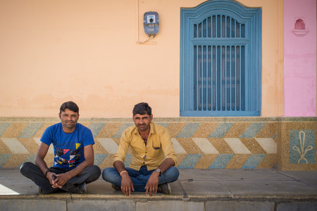 GODWAR REGION, INDIA - 15 FEBRUARY 2015: Two typical modern Indian men sit cross-legged on ground in front of home.のeditorial素材