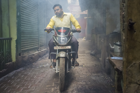 VARANASI, INDIA - 20 FEBRUARY 2015: Man on motorcycle passes through street filled with smoke. Coal ovens are used as source of heat for making milky tea.のeditorial素材