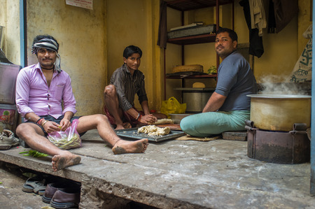VARANASI, INDIA - 20 FEBRUARY 2015: Three young adult men sit on ground and prepare lunch in simple kitchen.のeditorial素材