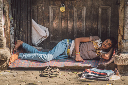 MUMBAI, INDIA - 10 JANUARY 2015: Young Indian man in street rests on mat in front of door. Post-processed with grain, texture and colour effect.のeditorial素材
