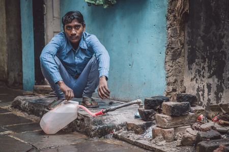 MUMBAI, INDIA - 12 JANUARY 2015: Young Indian man fills water tank in street. Dharavi slum mostly has drinkable water. Post-processed with grain, texture and colour effect.のeditorial素材