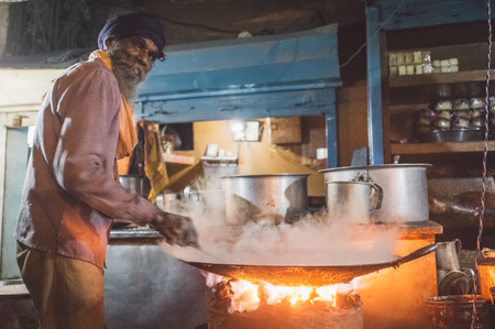 VARANASI, INDIA - 21 FEBRUARY 2015: Street vendor cooks meal in big pan on coal oven at night. Post-processed with grain, texture and colour effect.のeditorial素材