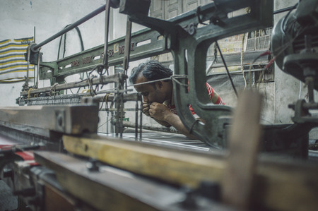 VARANASI, INDIA - 21 FEBRUARY 2015: Worker repairs textile machine in small factory. Post-processed with grain, texture and colour effect.のeditorial素材