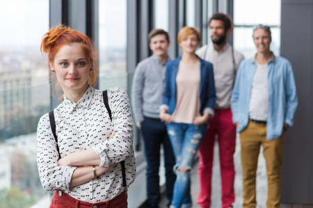 Corporate portrait of young red-head hipster business woman with her colleagues in background.の写真素材