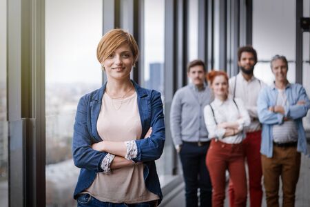 Corporate portrait of young business woman with her colleagues in background. Post processed with vintage film and sun filter.の写真素材