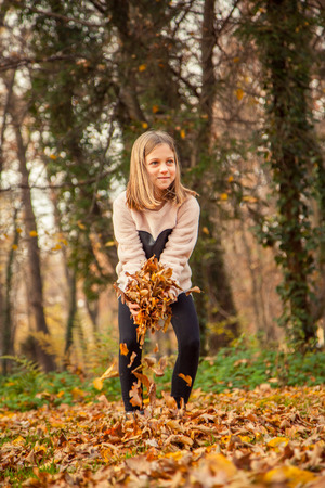 ZAGREB, CROATIA - 15 NOVEMBER 2015: Cheerful child, with heart shaped shirt, plays with leaves in park on an autumn day.の写真素材