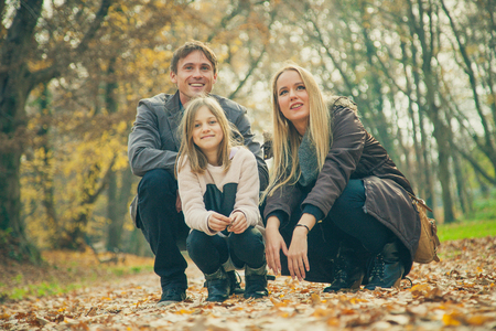 Family of three kneel in park on an autumn day.の写真素材