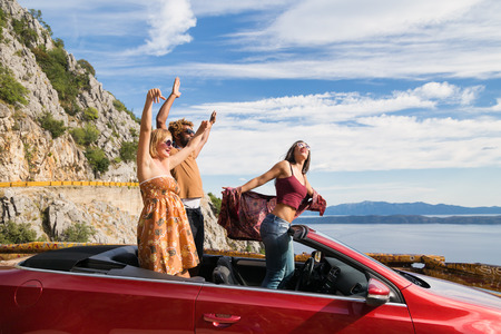 Group of happy young people waving from the red convertible.の写真素材