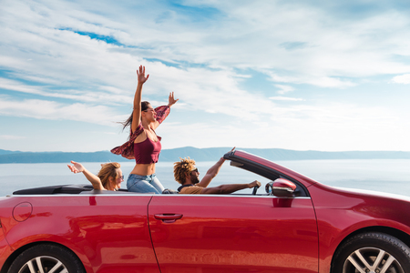 Group of happy young people waving from the red convertible.の写真素材