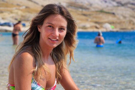 Beautiful tanned girl in a bikini sitting on a rocky beach.の写真素材