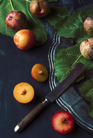 Plums pieces in dark table with green leafの写真素材