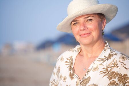 Portrait of a elegant mature woman wearing a hat enjoying the sunshine on a summer beach