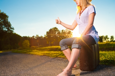 Pretty young woman hitchhiking along a countryside road during sunset, vintage mood picture with sunset lens flareの写真素材