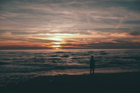 woman standing and looking at the sunset and the seaの写真素材