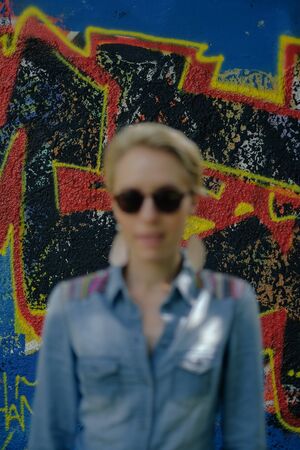 young woman with stylish sunglasses standing in front of a graffiti wall, focus is on the wallの写真素材