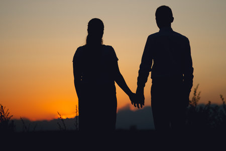 Silhouette of a couple in love walking together at sunset in summer. Romantic scene of lovers.の写真素材