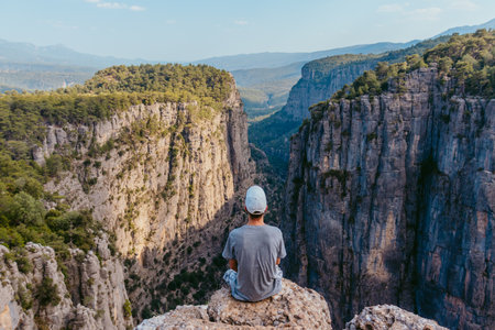 A guy in a cap and T-shirt sits looking at the panoramic landscape of lazi Kanyonu (Eagles Canyon) and Bilgelik Vadisi (Wisdom Valley). Koprulu Canyon National Park, Antalyaの写真素材