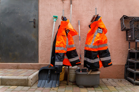 Bright orange uniform for outdoor work with reflective inserts hang on the wall near the tools.の写真素材