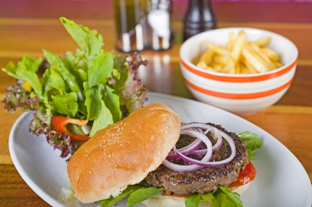 Beef burger in a bun with a side salad and dish of friesの写真素材